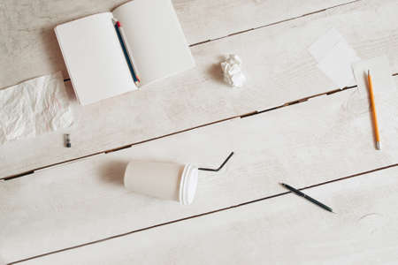 Workplace of untidy students flat lay, free space. Top view on blank copybook, pencils, coffee-to-go cup and paper wads scattered on white wooden table. Mess, disorder, bad form conceptの写真素材