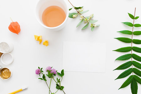 Blank card with plants and cup of tea flat lay. Top view on artisan table prepared for craft creating, herbarium decoration, free space. Art, inspiration of nature, art, hobby conceptの写真素材