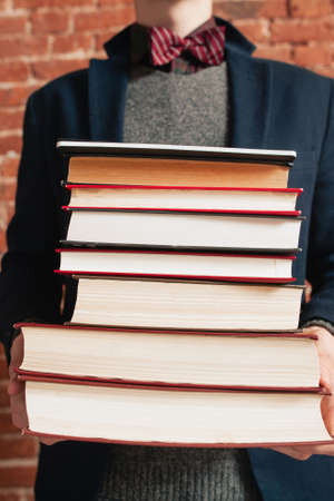 Unrecognizable man holding stack of books. Man in bow-tie standing with big pile of old textbooks. Science, education, information, knowledge conceptの写真素材