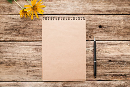 Brown sketchbook on old wood flat lay mockup. Top view on vintage notebook with pen and bright yellow flowers on grunge wooden background. Art, inspiration, imagination, planning conceptの写真素材