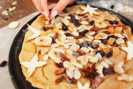 Decorating holiday pie with dry fruits close-up. Female hand preparing sweet treat for family, cooking process. Homemade bakery, valentines pastry, love, hobby, surprise conceptの写真素材