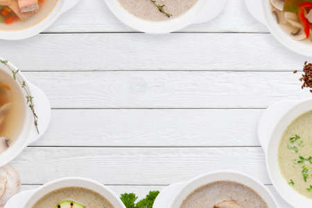 Different tasty soups frame on white wood flat lay. Top view on empty wooden table with variation of restaurant hot dishes. Worldwide cuisine, healthy food, buffet, lunch, menu conceptの写真素材