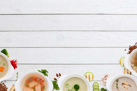Empty wooden table with variation of soups flat lay. Top view on white wooden background with different restaurant hot dishes, free space. Worldwide cuisine, healthy food, buffet, lunch, menu conceptの写真素材