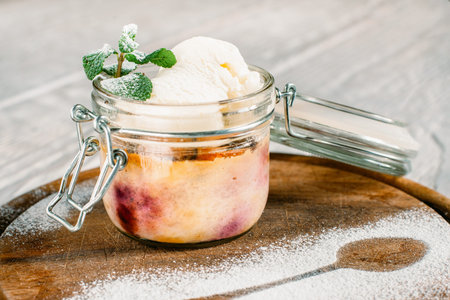 Delicious dessert served in glass jar on wood. Colorful sweet with ice cream on catering platter with teaspoon contour made with sugar powderの写真素材