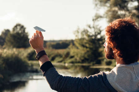 Man running paper airplane to river back view. Guy disporting with paper plane at nature, free space. Rest, entertainment, leisure conceptの写真素材