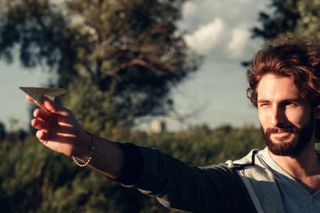 Profile of man aiming with paper airplane, free space on nature background. Young stylish guy launching note with his dream to air. Entertainment, leisure, pastime conceptの写真素材
