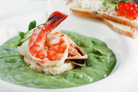 Broccoli cream soup with seafood close-up. Tasty spinach soup with shrimp and mussel, served with red caviar canape. Mediterranean cuisine, healthy food, restaurant menu conceptの写真素材