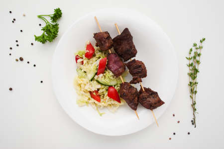 Appetizing shashlik with salad on plate flat lay. Top view on grilled pork sticks served with fresh vegetables. Healthy food, dinner, menu conceptの写真素材