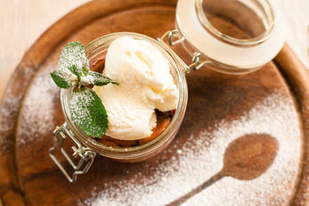 Ice cream in glass jar with mint top view. Sweet dessert served on wooden board decorated with sugar powder spoon contour. Restaurant serving, menu, summer conceptの写真素材