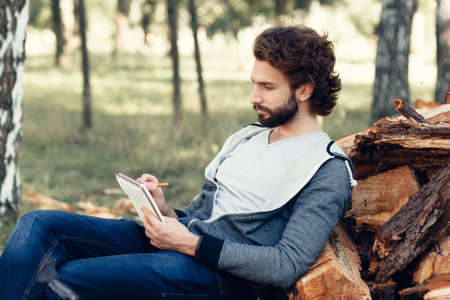Artist drawing landscape in notebook, side view. Young man creating at nature. Art, inspiration, idea, craft, leisure, hobby conceptの写真素材