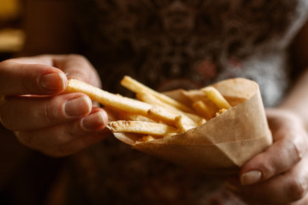French fries eating close-up. Unrecognizable woman taking fried potato from paper pack. Junk fast food, lunch time, snack, favorite recipe conceptの写真素材