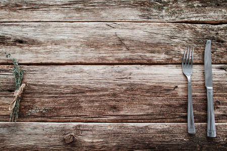Rustic wooden table with knife and fork free space. Top view on grunge rural background with cutlery and herbs, background for meal advertisement or restaurant menuの写真素材