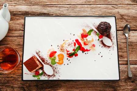 Variety of sweet desserts with tea and spoon flat lay. Top view on creatively decorated set of five kinds of cake with cup of hot drink, wooden background. Confectionery, restaurant menu conceptの写真素材