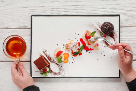 Sweet cakes mix eating, eater pov. Top view on man tasting desserts with cup of hot tea. Degustation, choosing dessert for party or wedding, gastronomy, event organization conceptの写真素材