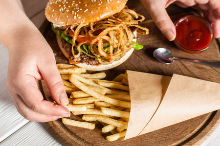 French fries eating top view. Hand taking fried potato from paper pack on tray with burger. American traditional cuisine, lunch time, fast junk food conceptの写真素材