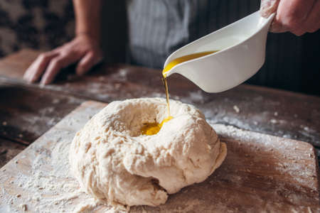 Adding olive oil to raw dough close-up. Baker preparing pastry for bread with all ingredients. Traditional bakery recipe, kitchen, cooking concept