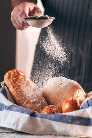 Sprinkling fresh bread with flour close-up. Baker decorating warm soft tack with sugar powder, free space. Homemade bakery, kitchen, cooking process conceptの写真素材