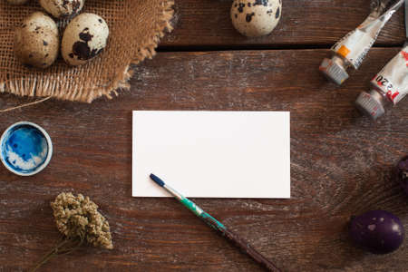 Blank greeting card with art tools flat lay. Top view on wooden table with empty paper, dye, paintbrush and egg. Handmade, art, Easter, tradition conceptの写真素材