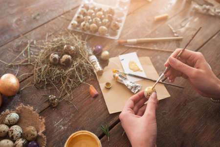 Woman coloring Easter eggs at home. Top view on female hands with egg and paintbrush, decorating eggs for holiday, artisan pov. Tradition, handmade, art conceptの写真素材