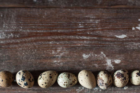 Quail eggs on wooden table flat lay. Top view on rustic background with line of raw eggs, free space for text. Easter, culinary, recipe, healthy food conceptの写真素材