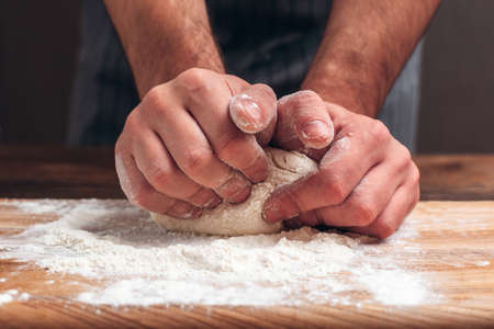Male hands kneading dough close-up. Baker man preparing pastry for bread, homemade recipe. Profession, bakery, culinary conceptの写真素材