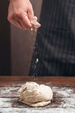 Baker sprinkling flour above raw dough. Cook preparing pastry, adding ingredients by recipe. Homemade bakery, cooking process conceptの写真素材