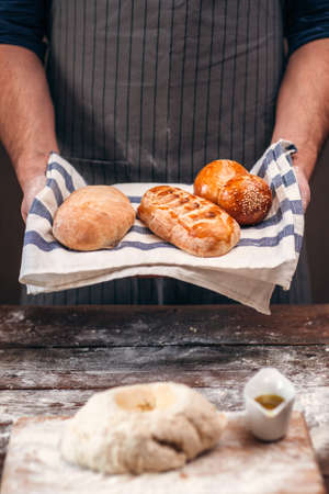 Man holding warm crusty bread above dough free space. Unrecognizable baker standing with made bread near raw pastry, presentation of new recipe, homemade bakery conceptの写真素材