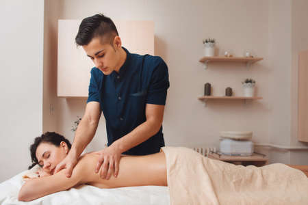 Chiropractor diagnosing woman at office free space. Young male masseur making treatment massage for nude brunette with pain in back. Health, beauty, body care conceptの写真素材