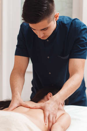 Serious masseur massaging female back closeup. Young man making treatment or relaxing procedures for nude woman. Beauty, health, rest, spa, body care conceptの写真素材