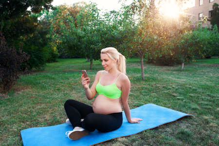 Smiling woman chatting on smartphone outdoor. Expectant female networking while resting at nature. Relax, pregnancy, communication conceptの写真素材