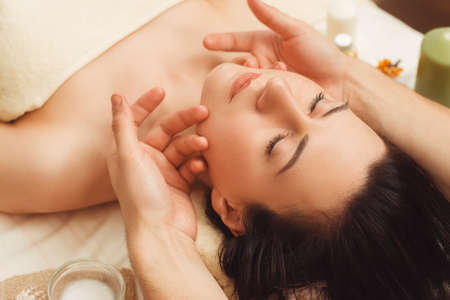 Portrait of young woman enjoying face massage. Closeup of beautiful woman relaxing under professional masseur hands. Body care, beauty, oriental spa, pleasure, resort conceptの写真素材