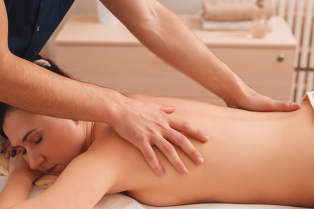 Masseur massaging nude woman free space. Side view on relaxed girl enjoying massage at spa salon. Beauty, health care, rest, body conceptの写真素材