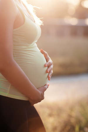 Pregnant woman in sunset in park, free space. Profile of unrecognizable expectant touching her belly. Pregnancy, love, maternity conceptの写真素材