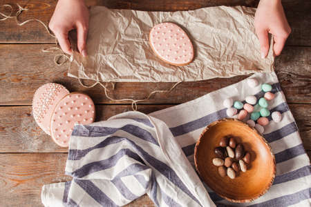 Packing sweet cookies for Easter flat lay. Top view on wooden table with egg form pink cakes and nuts, preparing treat for holiday. Tradition, dessert, sugar conceptの写真素材