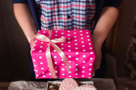 Unrecognizable woman holding pink gift box. Bright rosy present package in female hands, free space. Holiday, surprise, joy, fun conceptの写真素材