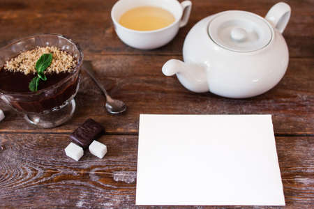 Blank card with teapot and dessert on table. Top view on wooden table with set for drinking tea and chocolate cream with white empty sheet of paper, free spaceの写真素材