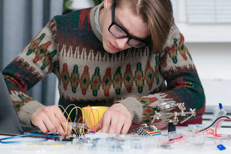 Young man intently working with electronic parts. Geek connecting colorful wires to breadboard at workshop. Electronic development, construction, diy, hobby conceptの写真素材