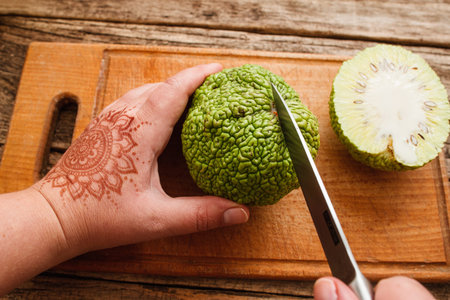 Woman cutting jackfruit on wooden board. Top view on female hand with mehendi picture carving green...