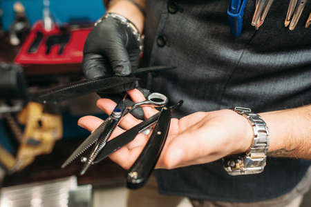 Barber instruments in hands closeup. Professional haircut tools - scissors, razor and hairbrush - in stylist hands, free space. Work, occupation, beauty, barbershop conceptの写真素材