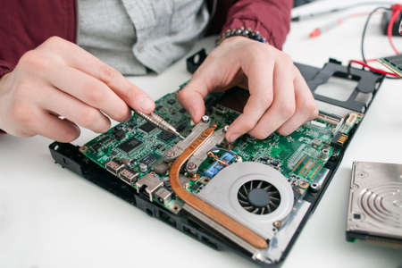 Disassembling computer motherboard closeup. Unrecognizable repairman screwing cpu in workshop with tools. Electronics construction, business conceptの写真素材