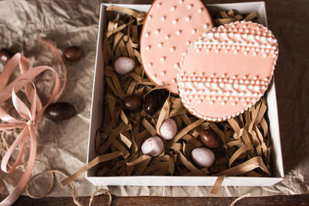 Egg form sweets in gift box close up. Cookies with pink glaze and chocolate eggs in package, traditional Easter treat. Confectionery, homemade pastry, seasonal, surprise conceptの写真素材
