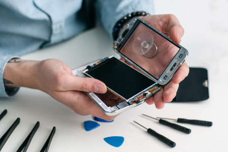 Repairman disassembling smartphone close-up. Male hands holding opened mobile phone for diagnostics, repair tools on workplace. Electronic fixing, modern technology, business conceptの写真素材
