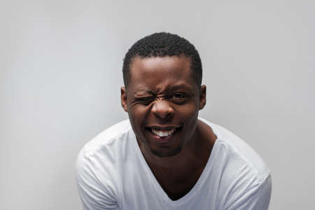 Smiling young african american man winking at the camera. Joy, happiness, laugh, good luck, great mood. Grey background with free space.の写真素材