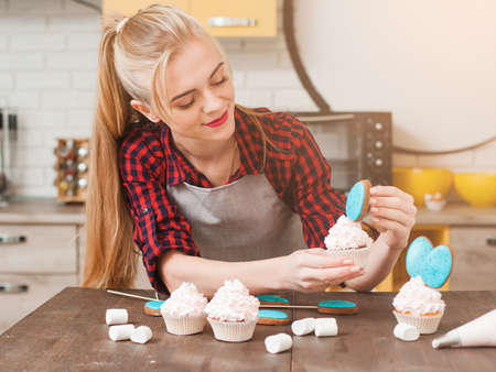 Girl decorating cup cakes with white cream and blue cake-pops at kitchen wooden table. Culinary masterclass. Easter gift, small business, delivery of sweets, craftmanship conceptの写真素材