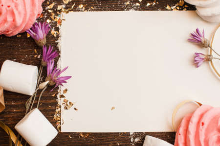 White empty sheet of paper for text framed with marshmallows, cookies, and flowers on rustic wooden tableの写真素材