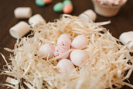 Small white sweet eggs in nest on wooden table closeup. Handmade decoration for easter celebration.の写真素材