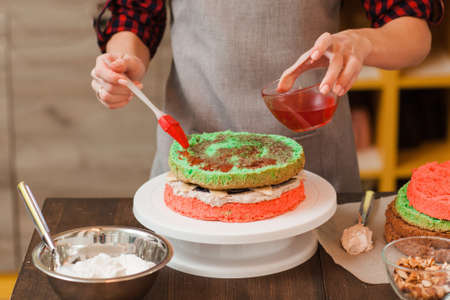 Masterclass of preparing color biscuit cake with white cream at home. Colorful bright festive food close up. Unrecognizable chef making creative birthday cakeの写真素材