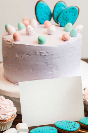 White decorated easter cake and cookies with a white blank card for text mockup. Gift, small business, culinary blog, good housewife, delivery of sweets conceptの写真素材