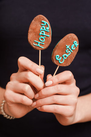 Woman hands holding two easter cake-pops with lettering isolated on black background. Easter greeting card conceptの写真素材