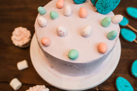 Beautiful adorned with cookies white biscuit cream easter cake placed on a plate on the wooden table. Closeup of festive sweet food.の写真素材